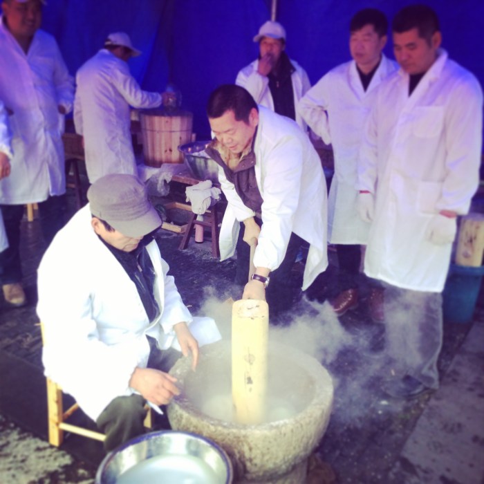 Here they are making the sticky rice by repeatedly pounding, rotating,  and smoothing the ball of rice with hot water until it is done. It is then formed into small cakes. 