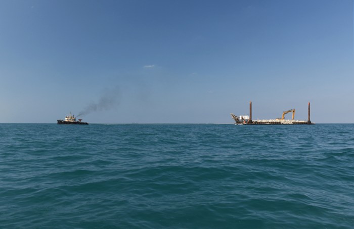 The construction both on land and in the Gulf is continuous and in every direction. Here a tugboat pulls a barge filled with bedrock.